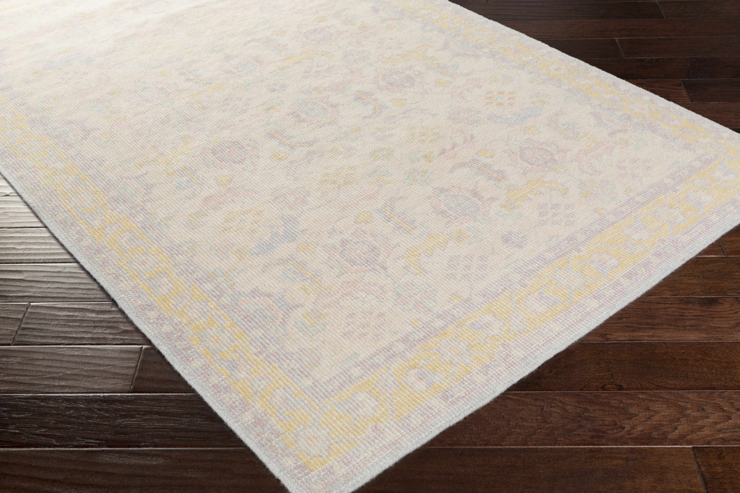 Close-up of the hand-knotted Navarino Area Rug, a traditional design in light beige, dusty pink, and mustard on dark wood floors. Corner