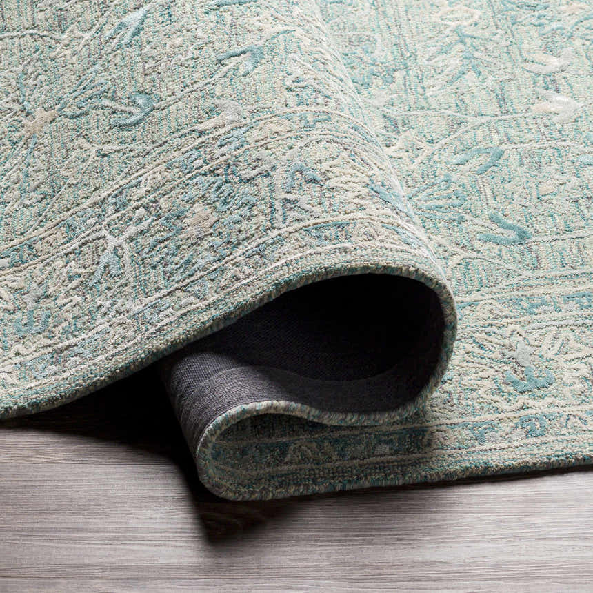 Close-up of the hand-tufted Neavitt Wool & Faux Silk Rug. Aqua, light beige, and gray tones with a traditional pattern. Fold