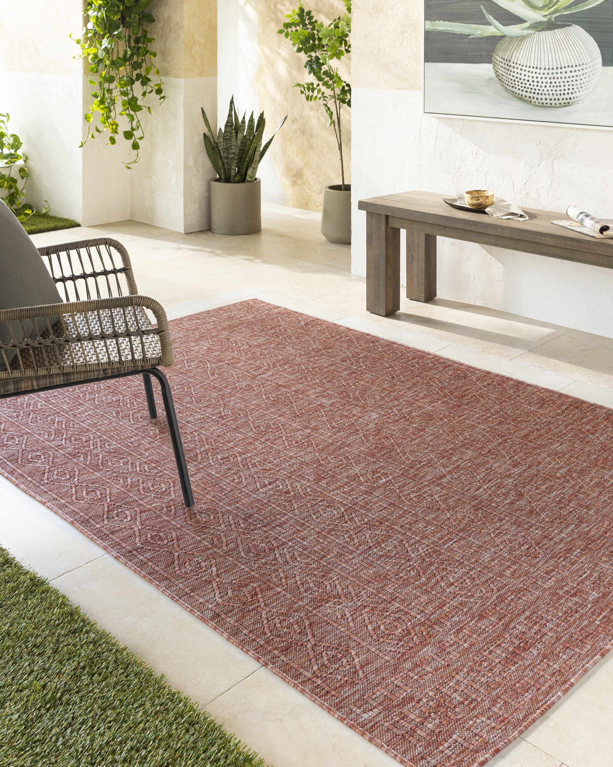 Outdoor patio scene with a Nuela Burgundy Area Rug, wicker chair, wood bench, and potted plants. Roomscene-Rectangle