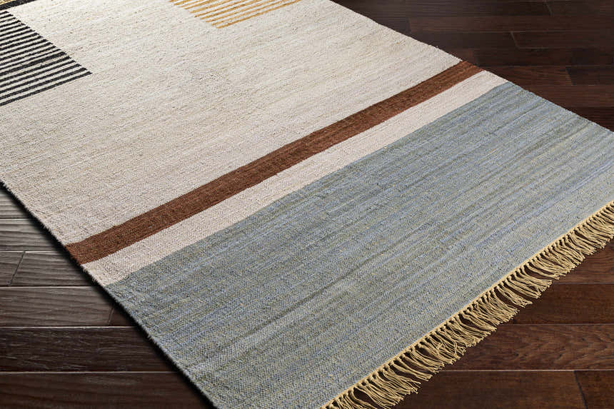 Close-up of the hand-woven Annangrove Area Rug. Beige, black, brown, and light blue stripes with tan fringe on dark wood floor. Corner