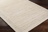 Close-up of the hand woven Nimue Tan Area Rug showing its ivory, tan colors and subtle pattern. Corner