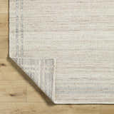 Close-up of the hand-woven Nimue Tan Area Rug. Ivory and tan wool rug with subtle stripes and a textured weave. Fold