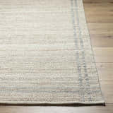 Close-up of the hand-woven Nimue Tan Area Rug showing its ivory and tan colors and subtle striped border. Front