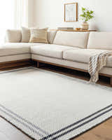 Living room scene with a Nimue Cream & Blue Bordered Area Rug, light wood floors, and a cream-colored sectional sofa. Roomscene-Rectangle