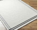 Close-up of the hand woven Nimue Cream & Blue Bordered Area Rug showing texture and striped border on wood floor. Corner