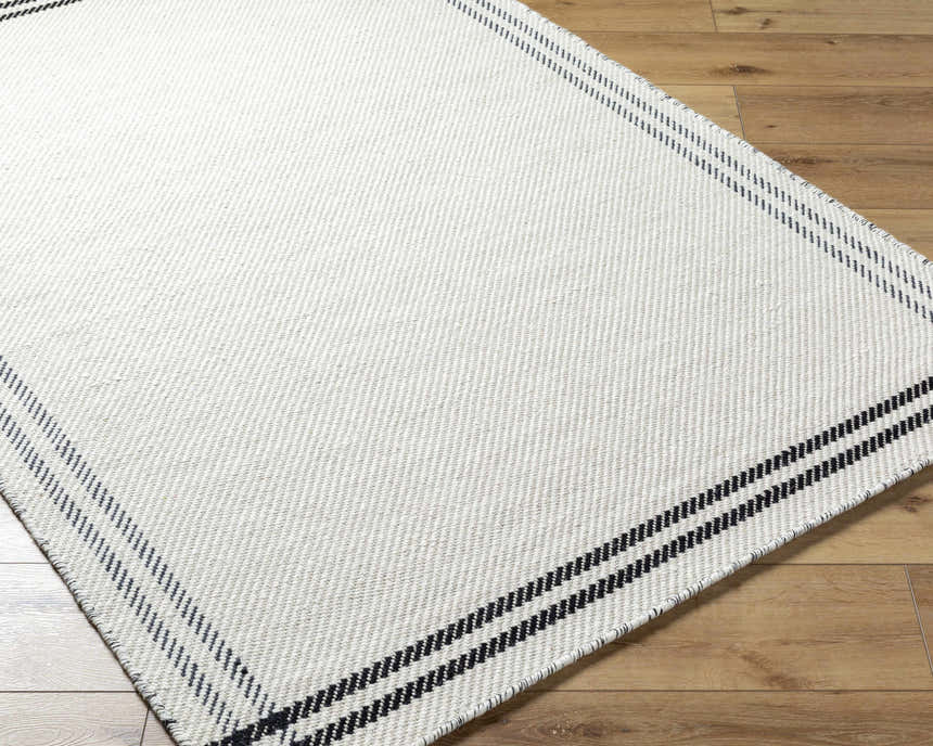 Close-up of the hand woven Nimue Cream & Blue Bordered Area Rug showing texture and striped border on wood floor. Corner