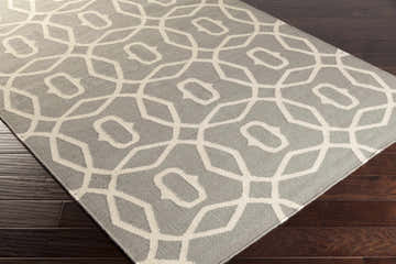 Close-up of the Norden Area Rug, a gray wool rug with a geometric cream-colored pattern on dark wood floors. Corner