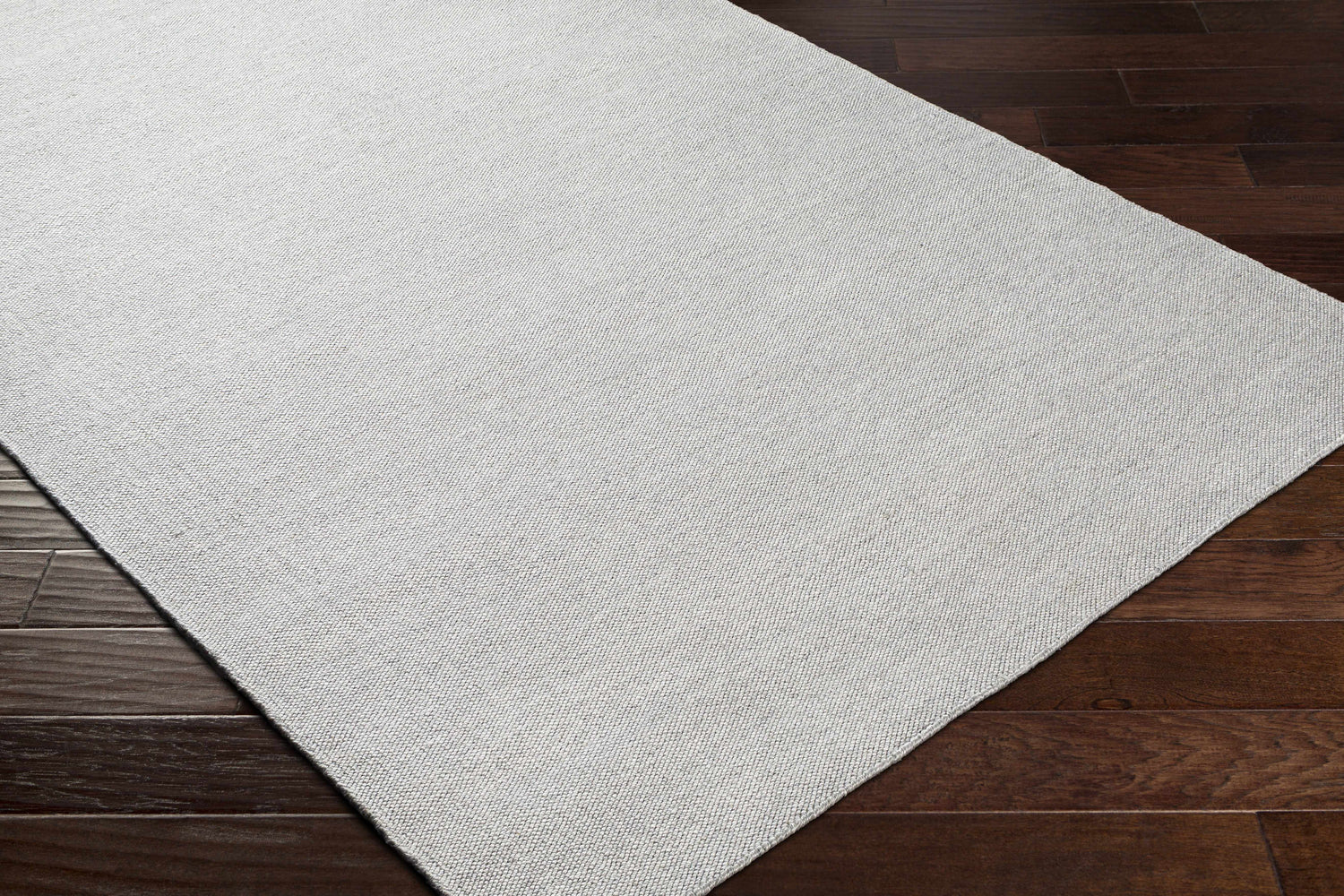 Close-up of the light gray Northop Indoor & Outdoor Area Rug showing the hand-woven texture and recycled PET yarn on dark wood floors. Corner