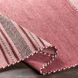 Close-up of the hand woven Northorpe Area Rug. Features pink hues and a geometric pattern border. Farmhouse style. Fold