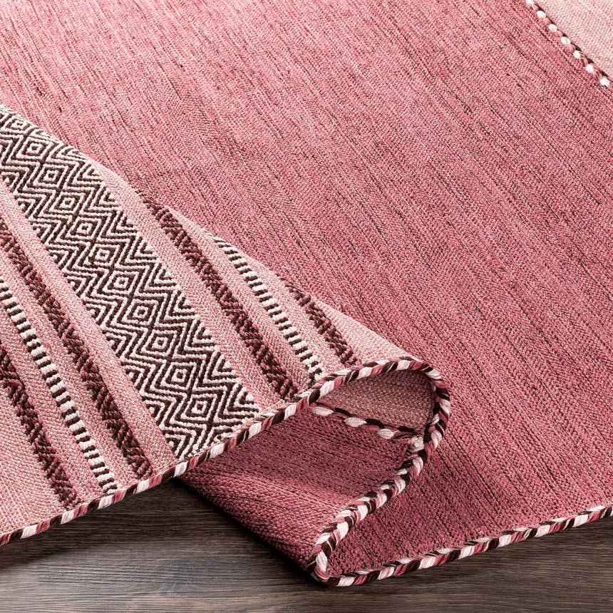 Close-up of the hand woven Northorpe Area Rug. Features pink hues and a geometric pattern border. Farmhouse style. Fold