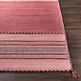 Close-up of the hand woven Northorpe Area Rug. Features pink hues, geometric patterns, and braided tassels. Front