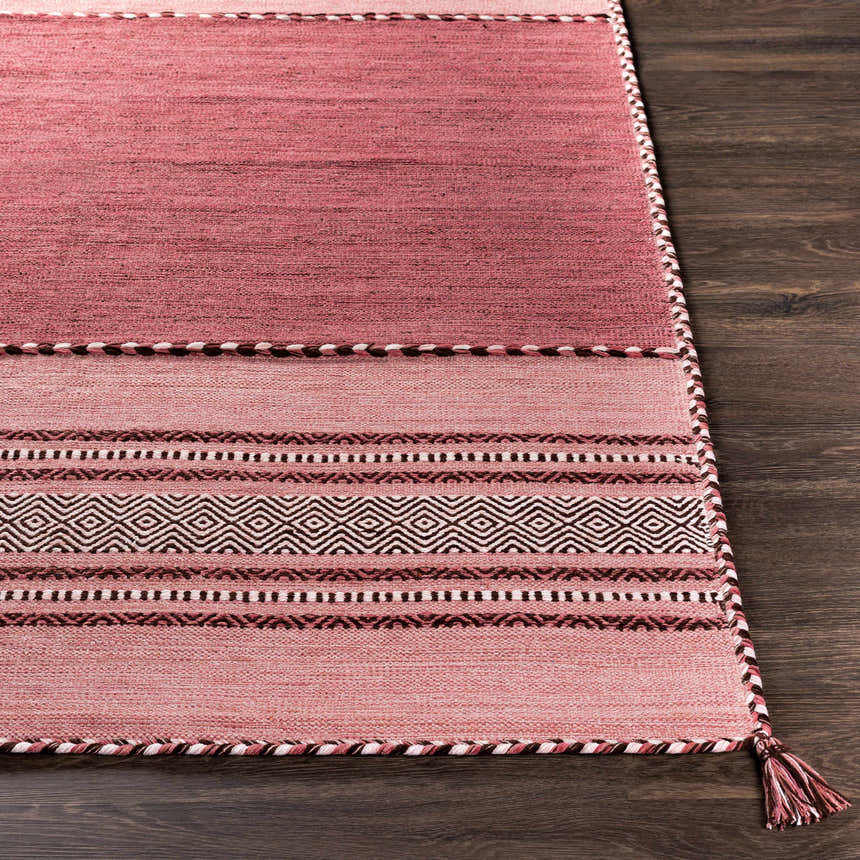 Close-up of the hand woven Northorpe Area Rug. Features pink hues, geometric patterns, and braided tassels. Front