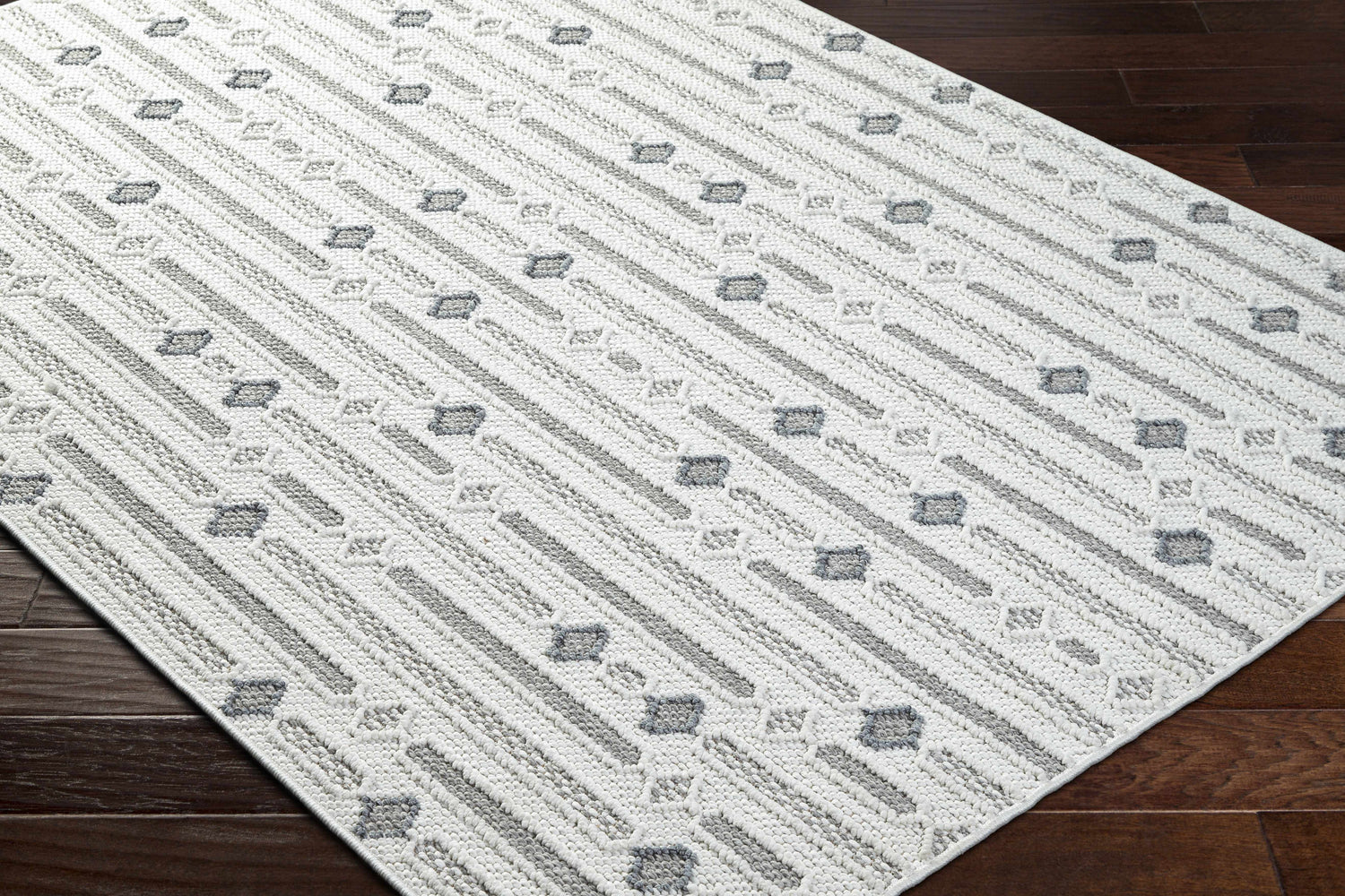 Close-up of Niara Area Rug. Contemporary style with ivory, light and medium gray stripes and geometric shapes. Corner