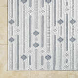 Close-up of the Niara Area Rug. Ivory, light gray, and medium gray geometric pattern. Machine woven polyester rug. Corner