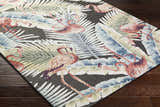 Close-up of Nayan Charcoal Area Rug with flamingo and palm leaf design in blue, cream, olive, and rust on dark wood floor. Corner