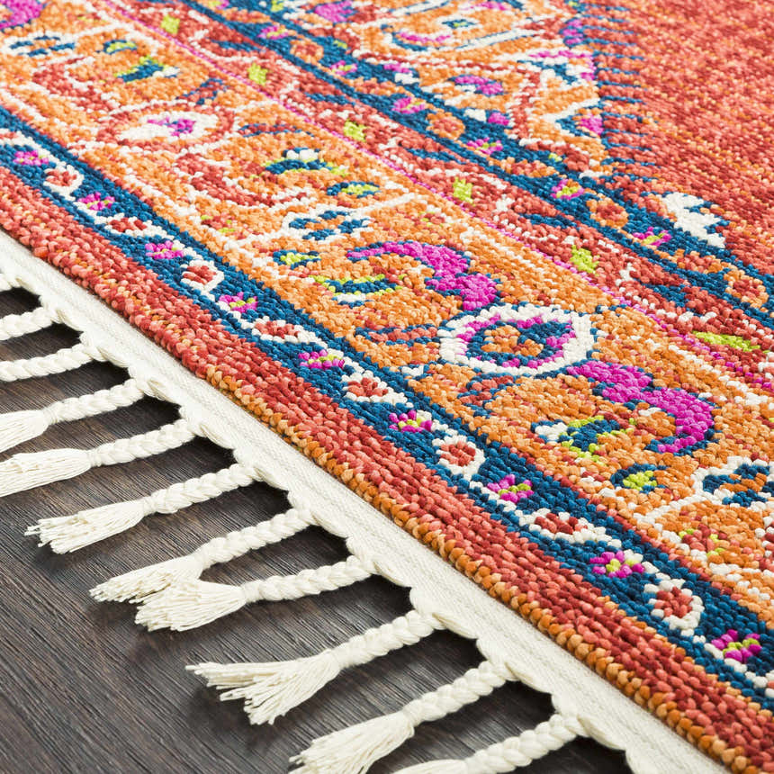 Close-up of the Oban Traditional Rug showing camel, coral, and blue hues, plus a detailed pattern and braided fringe. Texture