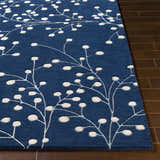 Close-up of the Blue Elsu Area Rug, a hand-tufted wool rug with a floral pattern in ink blue and tan on dark wood floors. Front