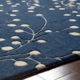 Close-up of the Blue Elsu Area Rug showing its ink blue wool texture and tan floral design on a hardwood floor. Texture