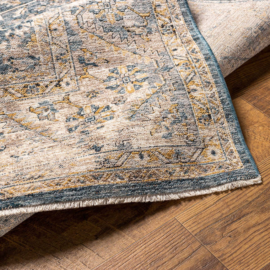Close-up of the Odala Luxe Performance Rug showing its traditional design, denim blue, beige, and mustard colors. Fold