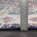 Close-up of Okarche Area Rug showing texture and pile height with ruler. Colors: beige, teal, navy, burgundy, and mustard. Pile