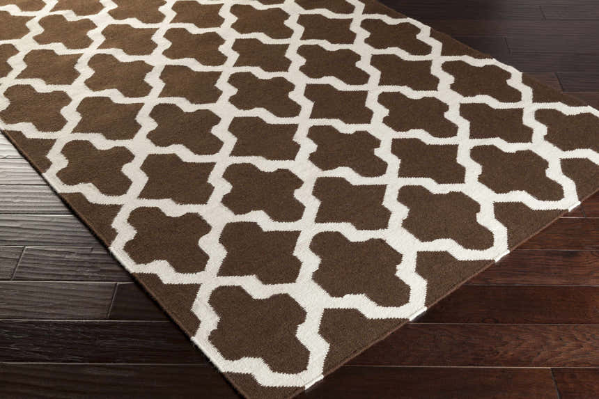 Close-up of the Okoboji Area Rug. Brown and ivory wool rug with a geometric quatrefoil pattern on dark wood floors. Corner