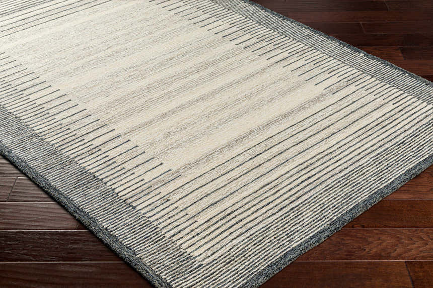 Close-up of the Omeo Wool Area Rug. Bone and dark gray stripes create a modern, Scandinavian design. Hand-tufted texture. Corner