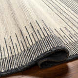 Close-up of the hand-tufted Omeo Wool Area Rug. Bone rug with dark gray, vertical stripes. Shows texture and binding. Fold