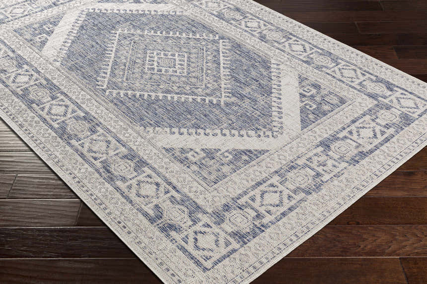 Close-up of the Umraniye Gray Area Rug showing its blue and off-white geometric, diamond, and square pattern. Corner