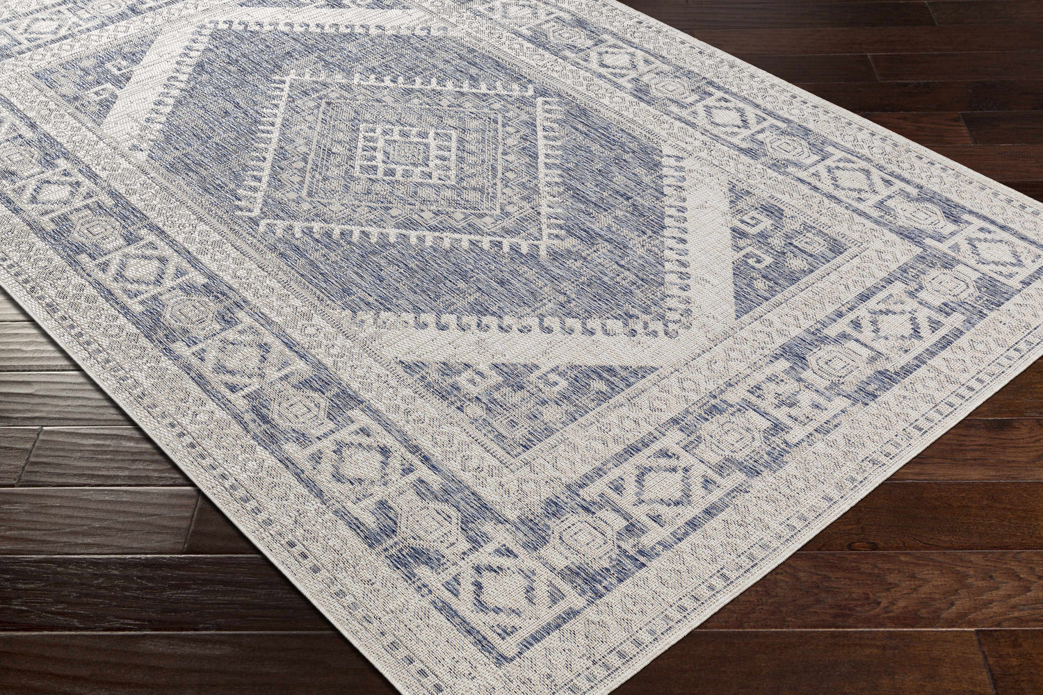 Close-up of the Umraniye Gray Area Rug showing its blue and off-white geometric, diamond, and square pattern. Corner