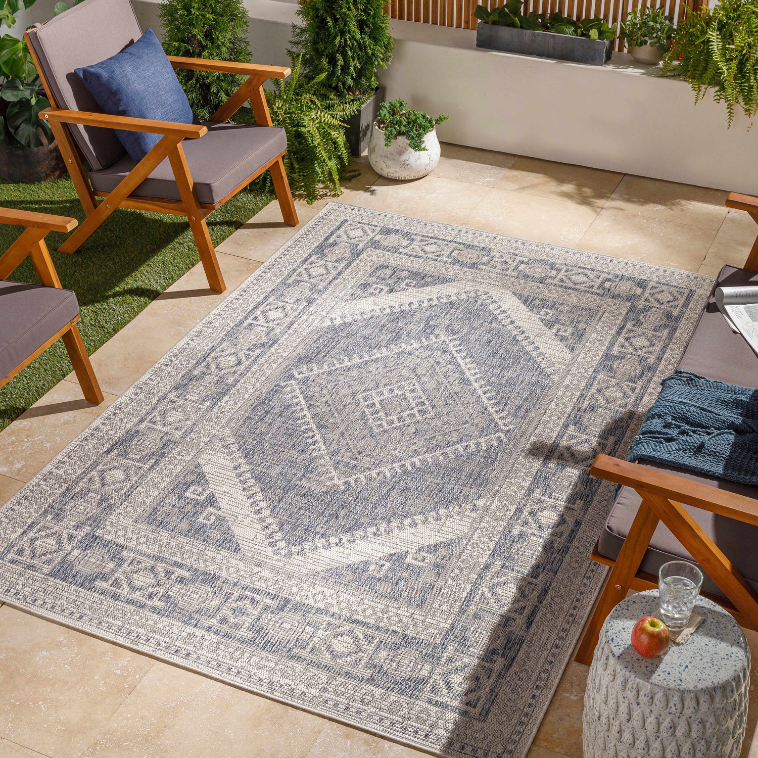 Outdoor patio with wood chairs and blue Umraniye Gray Area Rug. Coastal style with plants and tan tile. Roomscene-Rectangle