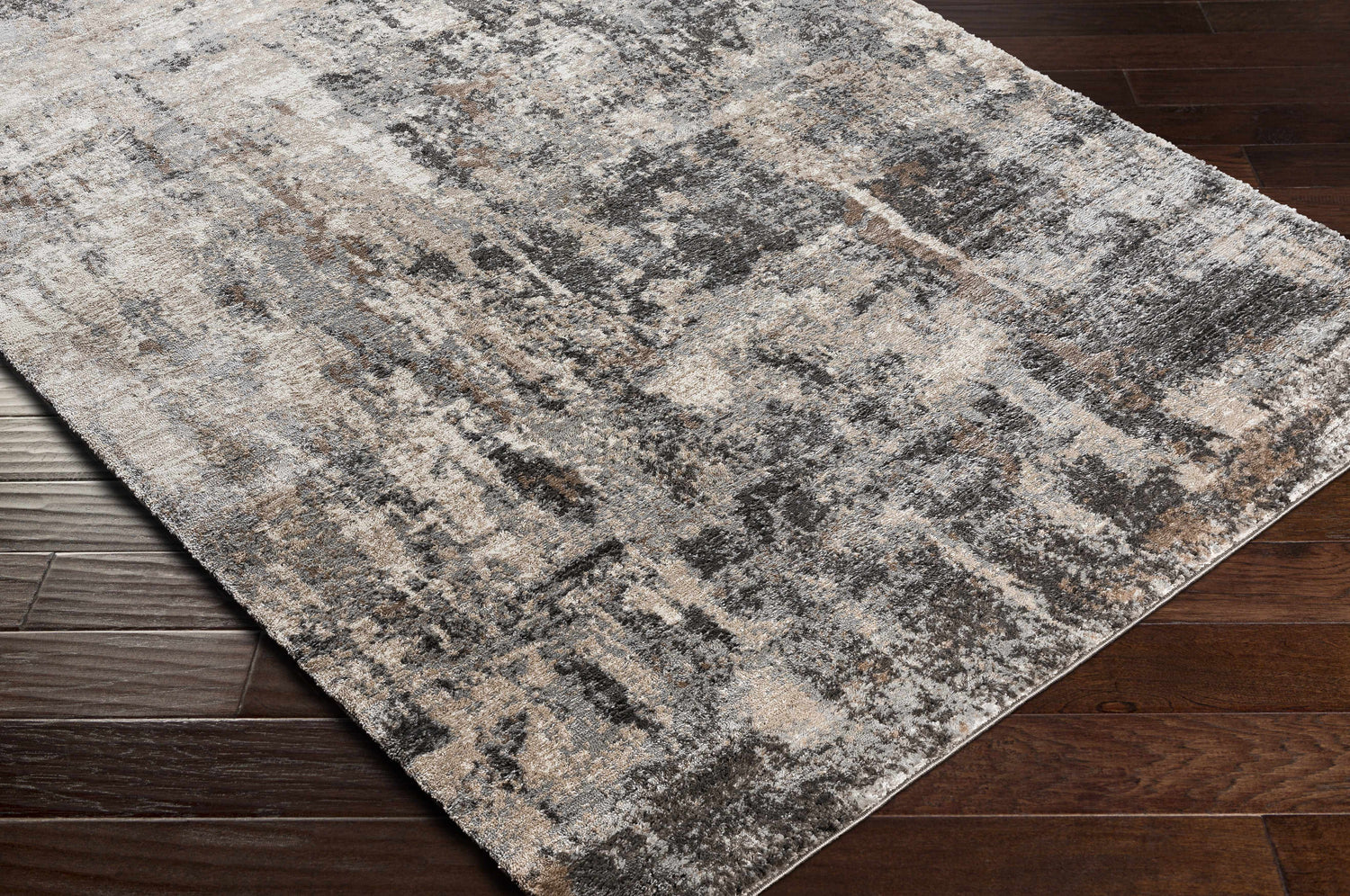 Close-up of the Opunake Luxe Thick Area Rug showing its abstract black, brown, cream, and gray pattern on dark wood floors. Corner