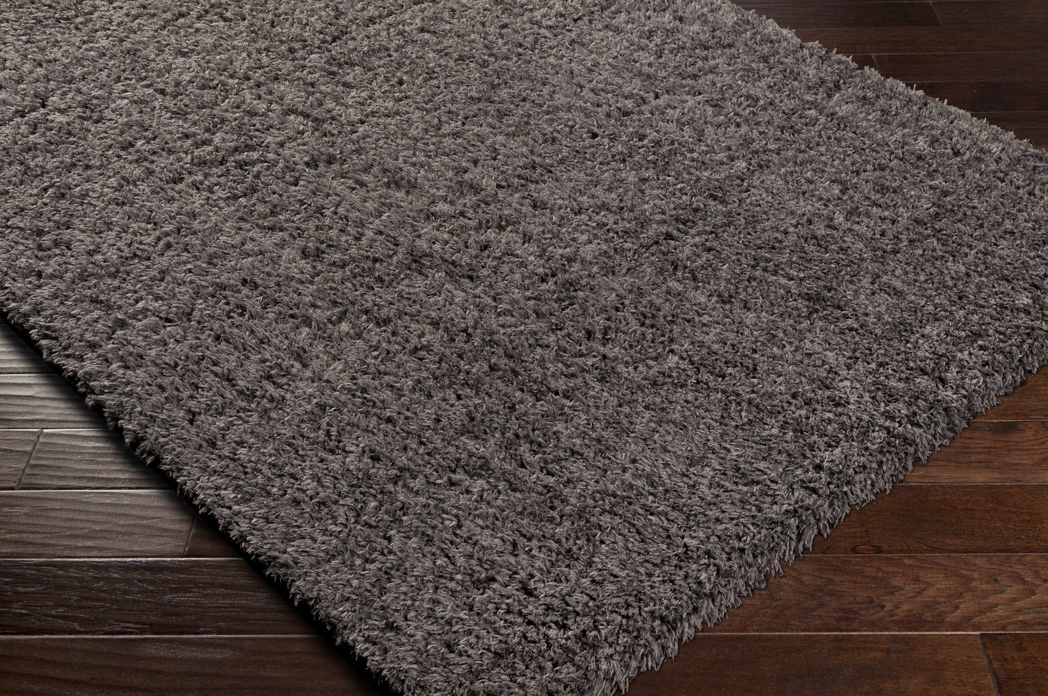 Close-up of the Siari Solid Charcoal Shag Rug showing its plush texture and dark gray color on a dark wood floor. Corner
