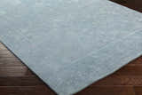 Close-up of the Oxly Area Rug showing a pale blue wool rug with a traditional floral pattern on dark wood floors. Corner