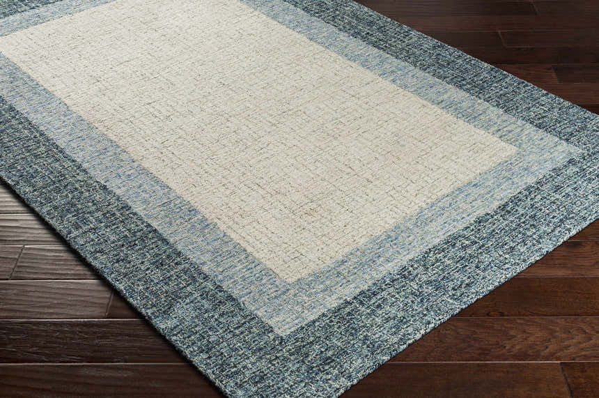 Close up of the Padada Green Bordered Cream Wool Rug showing texture and color variations of cream, light blue and navy. Corner