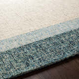 Close-up of a hand-tufted Padada Green Bordered Cream Wool Rug showing cream, light blue, and teal hues and wool texture. Texture