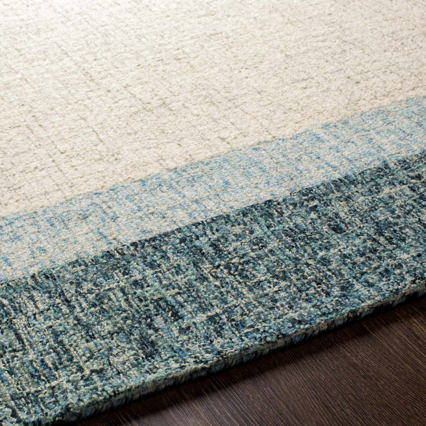 Close-up of a hand-tufted Padada Green Bordered Cream Wool Rug showing cream, light blue, and teal hues and wool texture. Texture