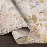 Close-up of the Palhi Area Carpet, a contemporary rug in cream, blue, gray, and mustard, with a machine-woven texture. Fold