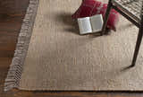 Close-up of the Partoun Area Rug showing its tan, jute texture and fringed edge, styled with a chair and book. Styleshot