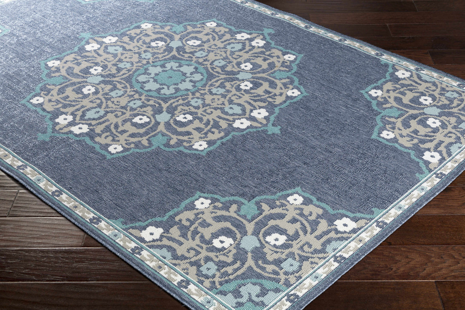 Close-up of Penland Area Rug. Navy rug with pale blue, taupe, and white floral medallion pattern on dark wood floor. Corner