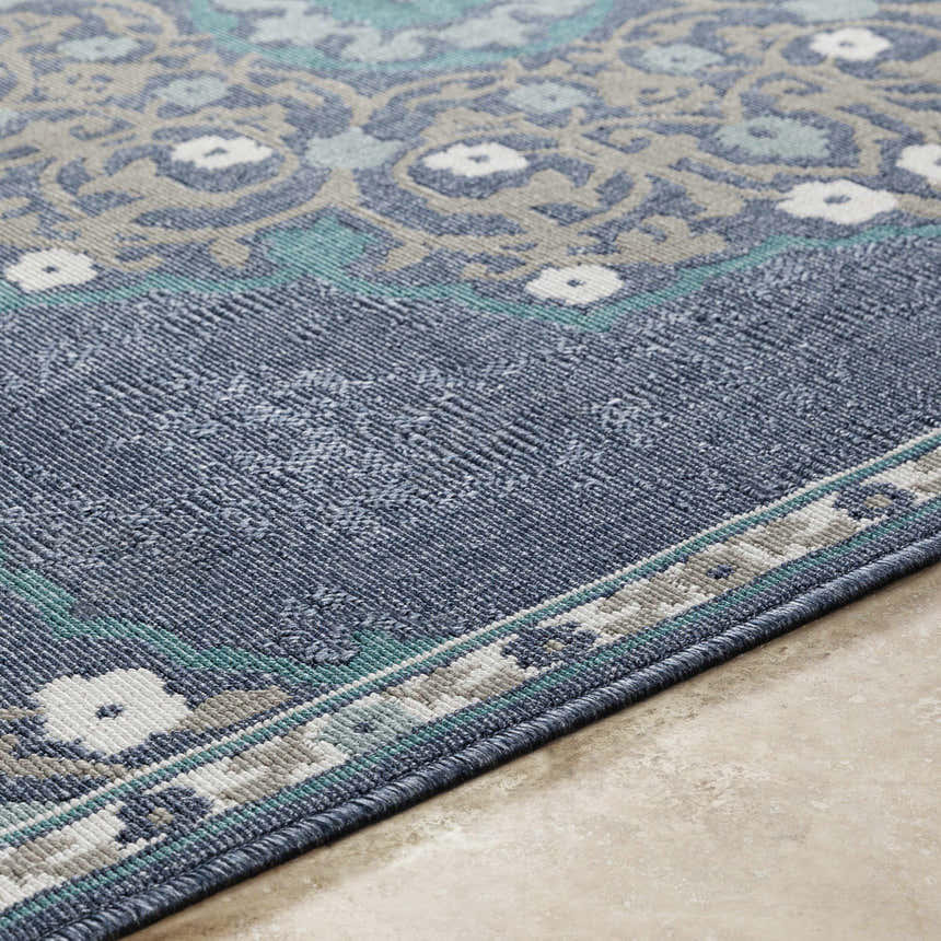 Close-up of the Penland Area Rug showing a navy, teal, taupe, and white floral pattern and machine woven texture. Texture
