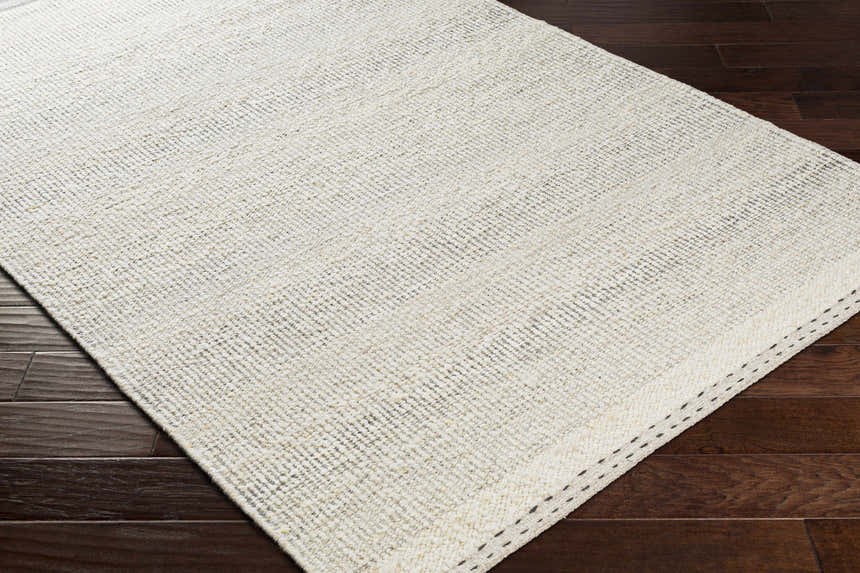 Close-up of the flat woven texture of the Penticton Cream Wool Rug on dark wood flooring. Corner
