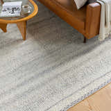 Living room scene with a brown leather couch and a Penticton Cream Flat Woven Wool Rug in beige, cream, and gray tones. Styleshot