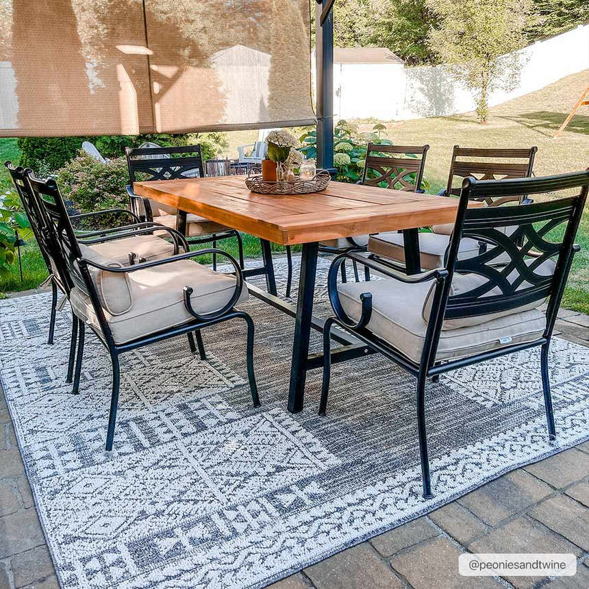 Outdoor patio scene with a wood table and black chairs on a gray and white Luddenham Textured Outdoor Rug. Roomscene-Rectangle