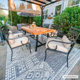Outdoor patio scene with wood table and black chairs on a Luddenham Textured Outdoor Rug in black, gray, and white. Roomscene-Rectangle