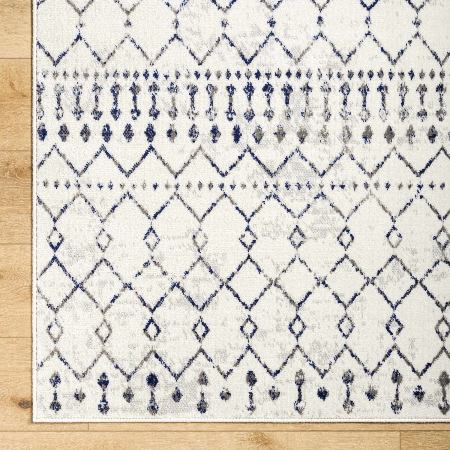 Close-up of Priel Area Rug: white rug with navy and gray diamond and tribal-inspired pattern. Bohemian style. Corner