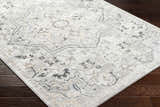 Close-up of the Phyre Area Rug in light gray, showcasing its traditional floral and geometric pattern on dark wood floors. Corner