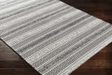 Close-up of the Planada Washable Area Rug. Black and cream cotton rug with a bohemian geometric pattern on dark wood floors. Corner