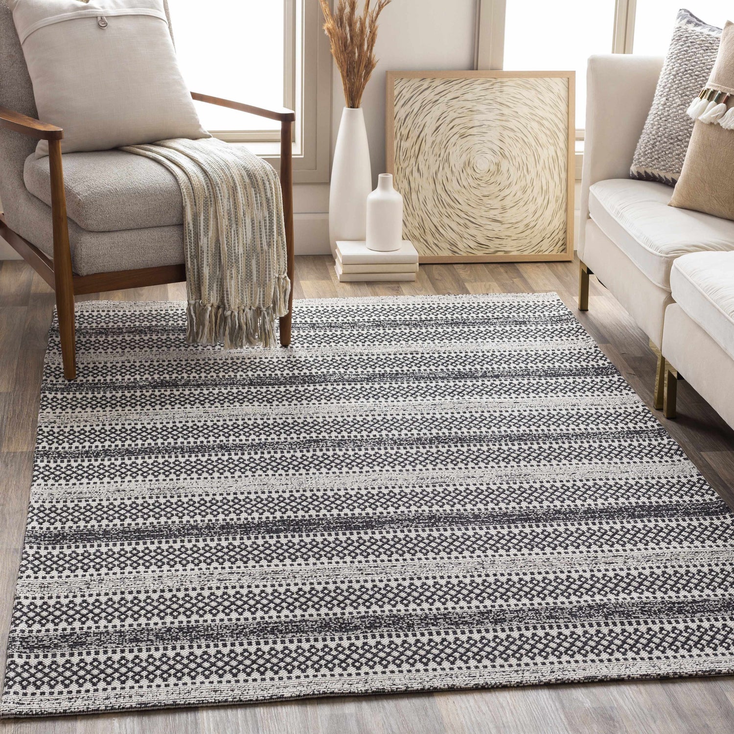 Living room scene with a black and cream Planada Washable Area Rug, sofa, chair, and neutral decor. Roomscene-Rectangle