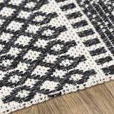 Close-up of the Planada Washable Area Rug. Black and cream geometric pattern, woven cotton texture on wood floor. Texture