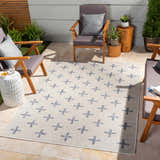 Outdoor patio scene with Pangao Area Rug in cream and navy, geometric pattern, surrounded by wooden chairs and potted plants. Roomscene-Rectangle